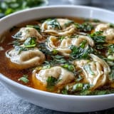 Hearty dumpling soup with tender chicken-filled dumplings in savory broth, garnished with fresh scallions for an aromatic touch.  