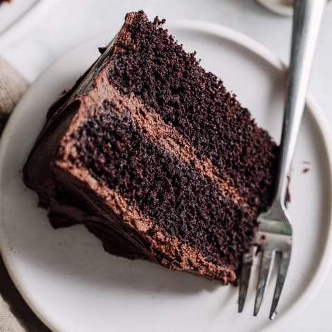A slice of moist layered Devil's Food Cake with rich chocolate buttercream frosting on a white plate.
