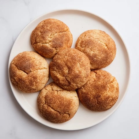 Stack of warm Snickerdoodles dusted with cinnamon sugar next to a glass of milk.
