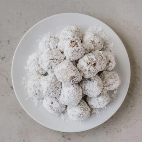 Mexican Wedding Cookies arranged on a rustic platter, their snowy powdered sugar coating catching soft light for a festive holiday spread.