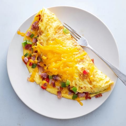 Savory Denver Omelet folded over melted cheddar, with sautéed ham, peppers, and onions on a rustic table.