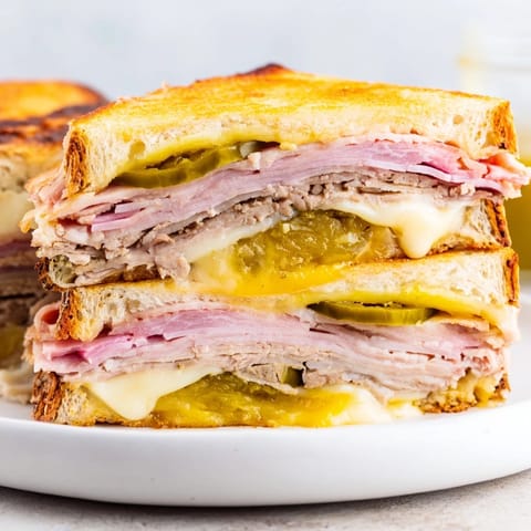 Golden, pressed Cuban Sandwich with pickles and mustard, sliced diagonally to reveal savory layers.