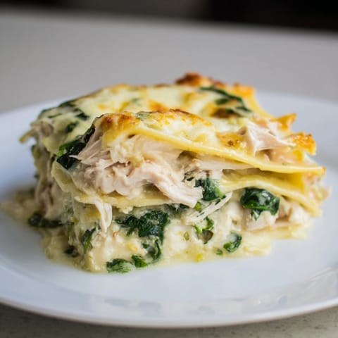 Hot slices of Chicken Alfredo Lasagna reveal tender chicken, spinach, and ricotta filling, served on a white plate for a cozy dinner.
