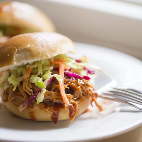 Juicy pulled BBQ chicken sliders topped with crunchy slaw and fresh cilantro on mini buns, ready to serve.