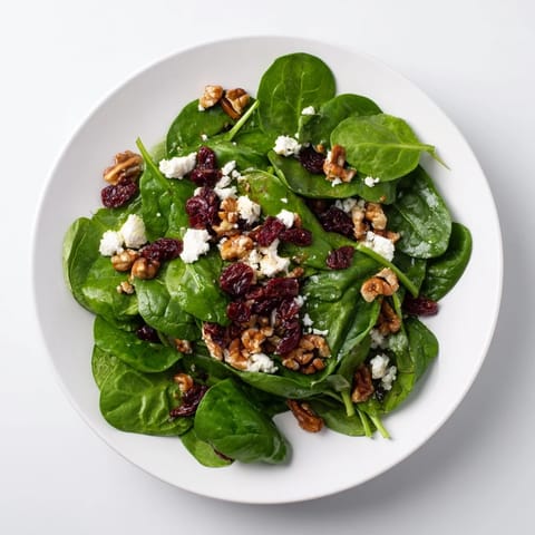 A close-up view shows the creamy goat cheese and ruby cranberries nestled in fresh spinach, with candied pecans adding a glossy, crunchy texture to the salad.
