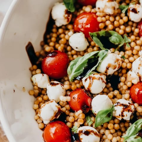 Fresh Caprese Couscous Salad in a white bowl, featuring juicy tomatoes, creamy mozzarella, and fragrant basil leaves, ready for a summer lunch.  