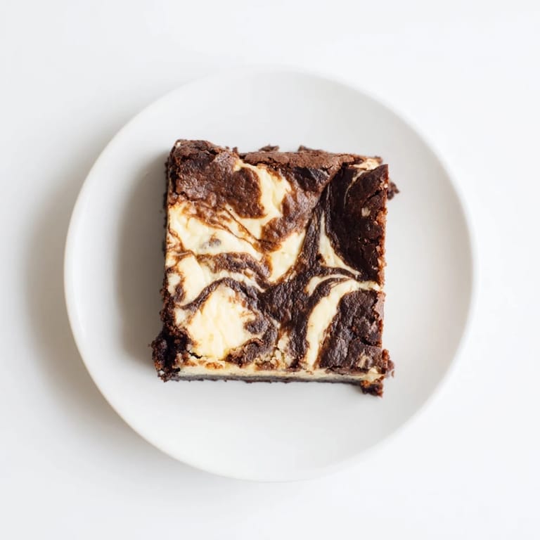 A square of Cheesecake Brownies being lifted from the pan, revealing its dense texture and indulgent chocolate and tangy cream cheese layers.