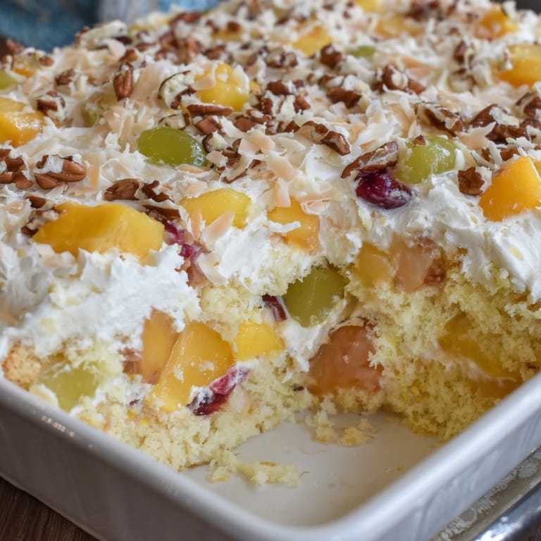 A close-up of Fruit Cocktail Cake showing tender fruit pieces and a glossy coconut frosting drizzle.