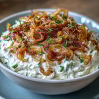 Creamy caramelized onion dip with Greek yogurt base, garnished with fresh chives and served with crispy potato chips.